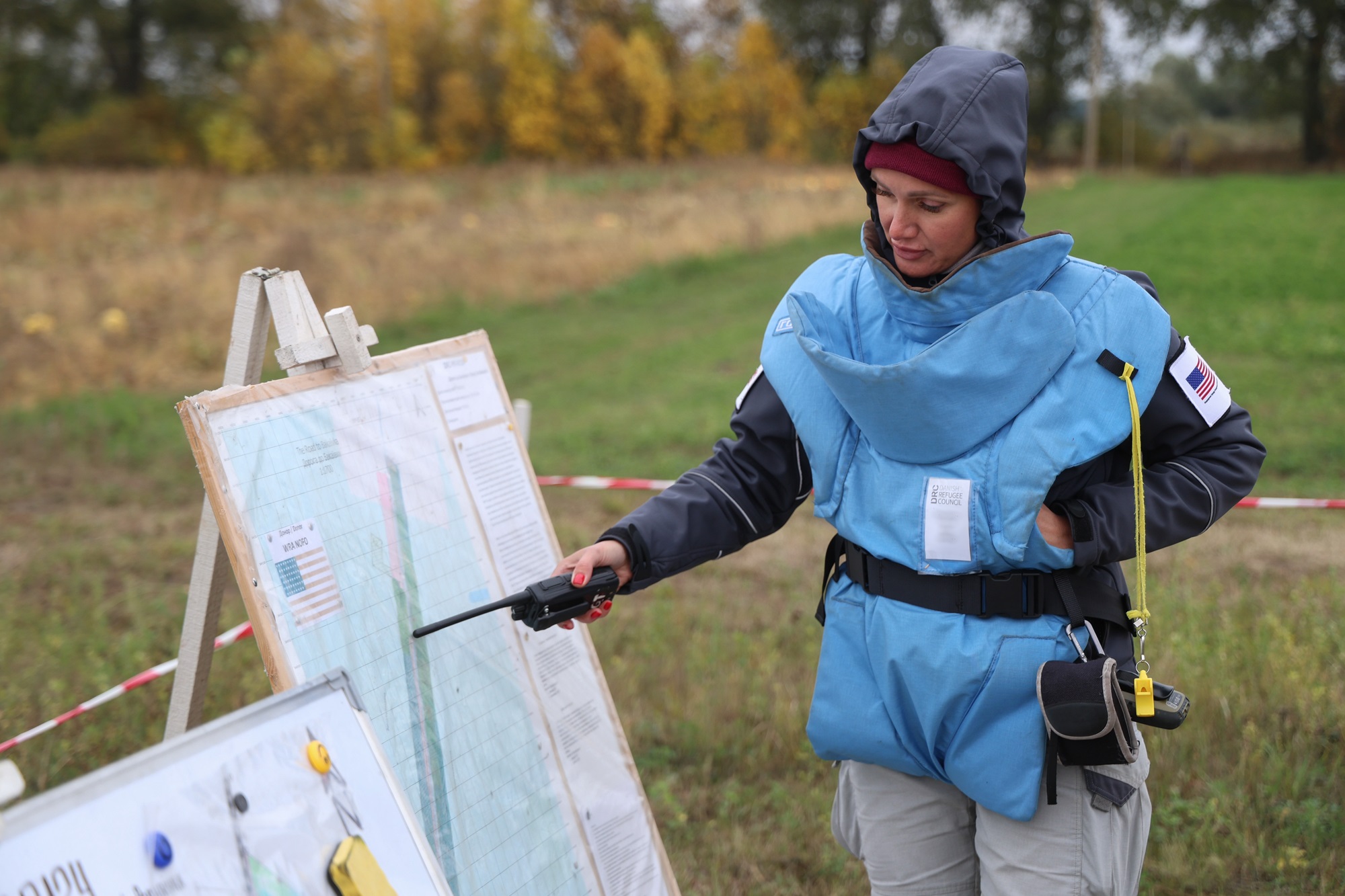 Olena, DRC Demining Team Leader, equipped with protective gear, reviews demining plans in a field.© DRC Ukraine, Dorohynka, Chernihiv Oblast, October 2024, Oleksandr Ratushniak