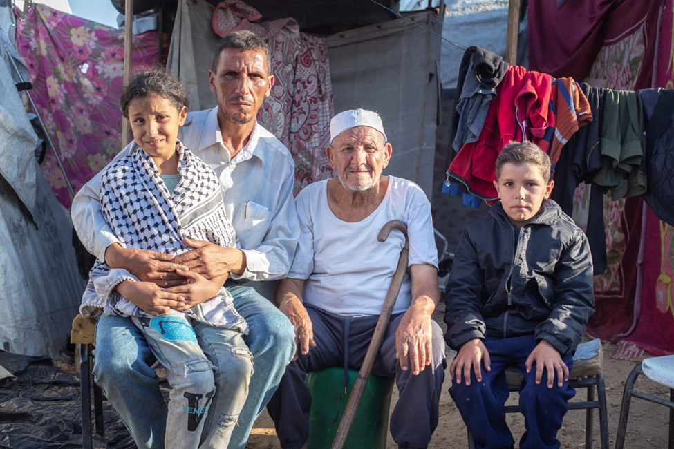 Shadi, a teacher from Jabalia sits in front of his tent with his father and two of his kids
