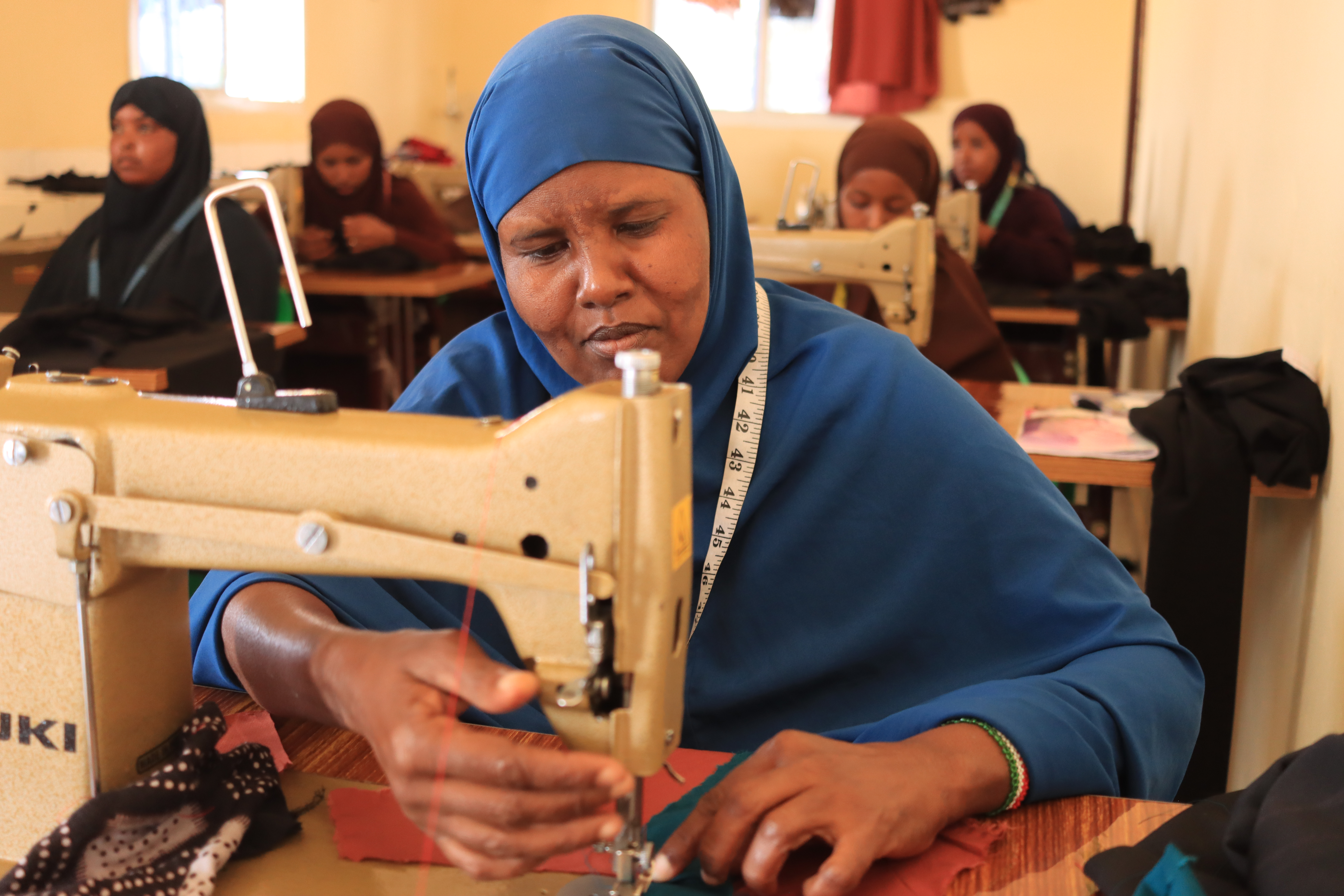 Rodo carefully measures and cuts fabric during a tailoring lesson, taking her first steps toward a skill she once only imagined learning.